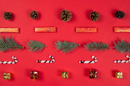 Christmas abstract pattern, flat lay. Fir tree branches, gift box and cone on red background. Concept of New Year presents, festive and holiday shopping. Top view.の写真素材