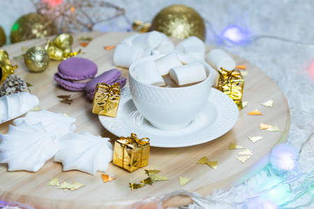 A cup of coffee with milk and marshmallows and garland on wooden salver, other sweets and Christmas decorations around. Concept of New Year presents, festive and holidayの写真素材