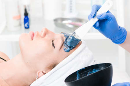 The young female client of cosmetic salon having a cleansing facial mask. The procedure of applying a peeling mask to the face. Concepts of skin care and beauty salon or clinic.の写真素材