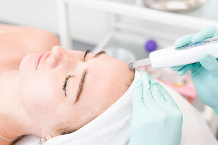 The female cosmetologist makes a procedure of ultrasonic cleaning face, close-up. Young woman in a beauty salon. Concept of cosmetology and professional skin careの写真素材