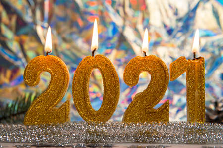 Burning golden candles 2021, close-up. Silver pine cones and branch are on the background. Concept...