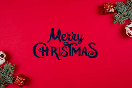 Merry Christmas lettering on red background, fir tree branches and New Years balls around, flat lay. Concepts of greeting card. Top viewの写真素材
