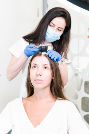 The doctor dermatologist examining client hair with a special apparatus for diagnostic hair. Trichoscopy procedure in the trichology clinic. Concept of health care.の写真素材