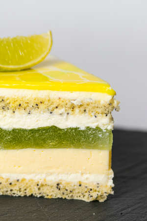 Close-up piece of mousse cake covered yellow mirror glaze with a slice of lime. French dessert. Frozen mirror icing on the cake. Baking and confectionery concept.の写真素材