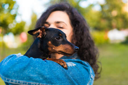 Young woman with her little dog outdoors. Black and Tan miniature pinscher female dog with owner in a parkの写真素材