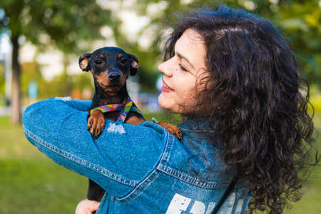 Young woman with her little dog outdoors. Black and Tan miniature pinscher female dog with owner in a parkの写真素材