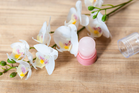 Natural eco crystal alum deodorant and orchid branch with flowers on light wooden background. Environmentally friendly lifestyle, personal hygiene and health care conceptの写真素材