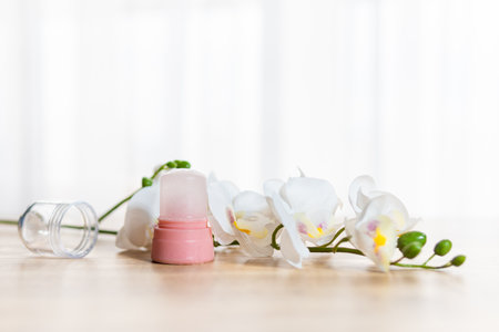 Natural eco crystal alum deodorant and orchid branch with flowers on light wooden background. Environmentally friendly lifestyle, personal hygiene and health care conceptの写真素材