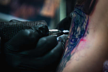 Professional tattoo artist makes a tattoo on a young man's hand, close-up. Tattoo artist doing tattoo in tattoo salon.の写真素材