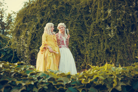 Portrait of two blonde woman dressed in historical Baroque clothes with old fashion hairstyle, outdoors. Luxurious medieval dressの写真素材
