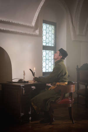 Portrait of a man in a medieval costume. A scribe writes on a red table. Retro style and historical clothing conceptsの写真素材