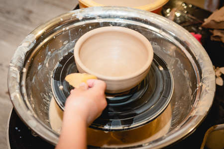 Potter working on potters wheel with clay. Process of making ceramic tableware in pottery workshop. Handicraft and art concept.の写真素材