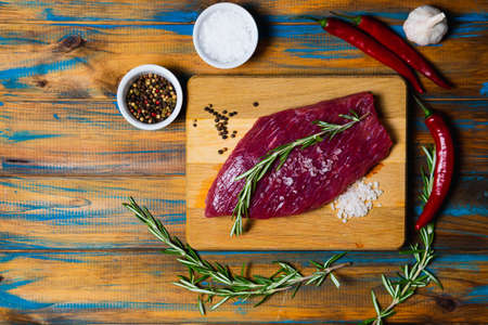Raw organic beef meat with rosemary, seasonings, salt and red pepper on wooden background. Preparation for barbecueの写真素材