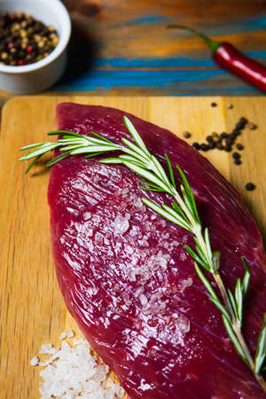 Raw organic beef meat with rosemary, seasonings, salt and red pepper on wooden background. Preparation for barbecueの写真素材