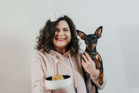 Happy young girl giving homemade cake to her dog, indoors. Concept of childfree by choice and celebrating dog's birthday partyの写真素材