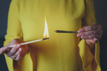 Close-up of adult woman lights up with matches and smoking medical marijuana joint. Concept of...