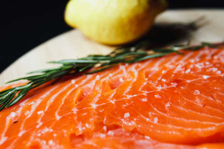 Fresh raw salmon fillet with seasonings and herbs, close-up on black background.