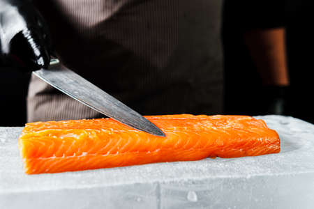 Close-up of chef hand prepared to cooking fresh salmon fillet, black background. Raw fish on the block of iceの写真素材