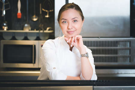 Portrait of confident and smiling young woman chef dressed in white uniform, professional kitchen...