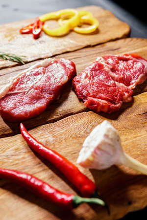 Raw organic beef meat with rosemary, seasonings, salt and red pepper on wooden cutting board, close-up. Preparing to cook steakの写真素材