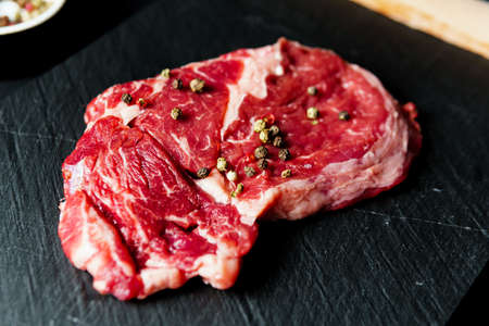 Raw organic beef meat with rosemary, seasonings, salt and red pepper on black background, close-up. Preparing to cook steakの写真素材