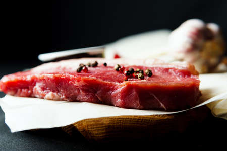 Raw organic beef meat with rosemary, seasonings, salt and red pepper on black background, close-up. Preparing to cook steakの写真素材