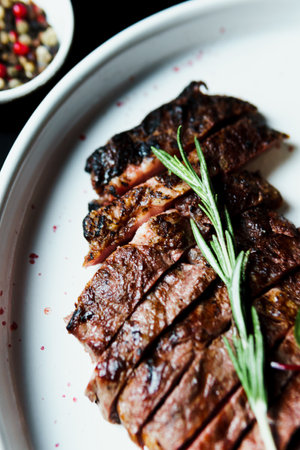 Sliced grilled steak medium rare served on white plate with vegetables. Delicious juicy meat in the...