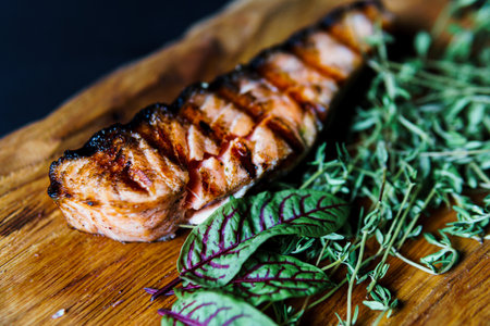 Grilled salmon fish fillet with green salad on the wooden cutting board, close up. Delicious food in the restaurant menu. Concept of catering serviceの写真素材