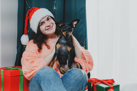 Portrait of young woman playing with funny dog miniature pinscher around Christmas ball and gift boxes. Concept of New Year moodの写真素材