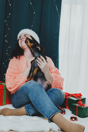 Portrait of young woman playing with funny dog miniature pinscher around Christmas ball and gift boxes. Concept of New Year moodの写真素材