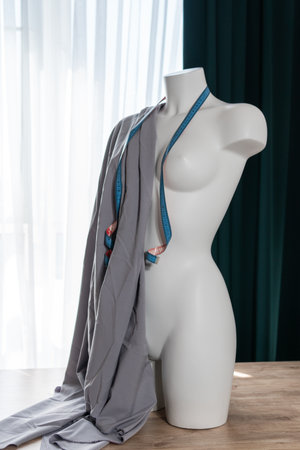 White modern mannequin or dressmakers dummy with gray fabric and hanging measuring tape, closeup. Concept of sewing workshopの写真素材