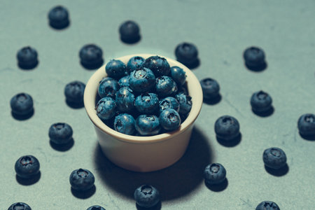 Freshly picked juicy blueberries in the bowl on blue background, close up. blueberry background. Concept of healthy nutrition, organic food. Vegan and vegetarianの写真素材