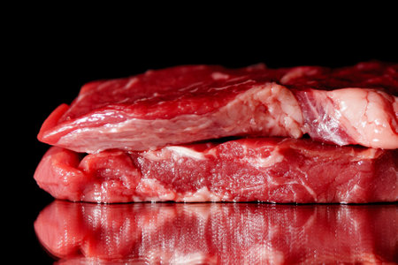 Raw organic beef meat with rosemary, seasonings, salt and red pepper on black background, close-up. Preparing to cook steakの写真素材