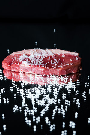 Raw organic beef meat with rosemary, seasonings, salt and red pepper on black background, close-up. Preparing to cook steakの写真素材