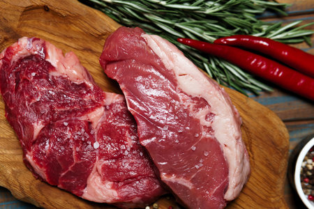Raw organic beef meat with rosemary, seasonings, salt and red pepper on wooden cutting board, close-up. Preparing to cook steakの写真素材