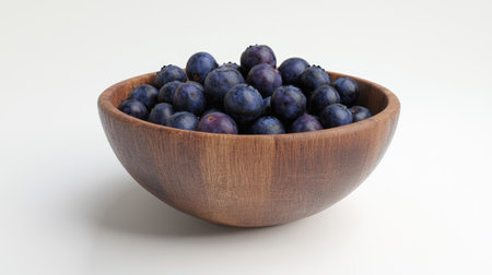 A round wooden bowl with fresh blueberries against a plain white background, exuding simplicity and freshness.の素材