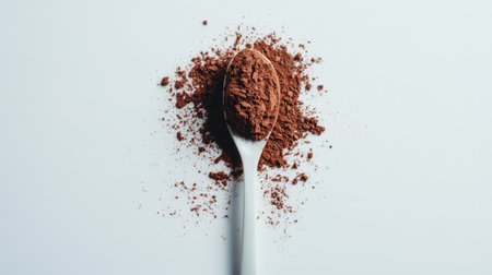 A teaspoon of cocoa powder placed upright, the powder spilling slightly on a white background for texture.の素材