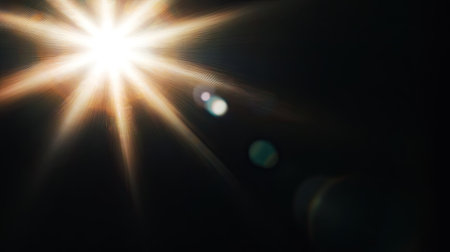 Intense sunlight glare with visible lens flare elements on a black background, perfect for atmospheric and moody designsの素材