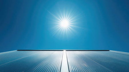 Solar panels installed on a slanted roof, perfectly aligned under a bright blue sky with the sun overheadの素材