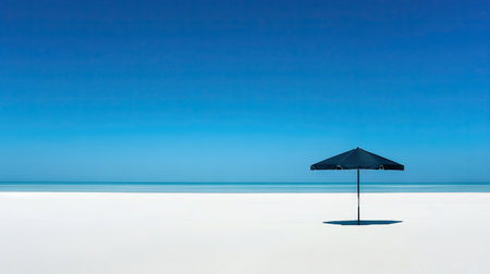 A solitary beach umbrella casting a shadow on the sand under the clear blue sky, evoking a peaceful vibe.の素材