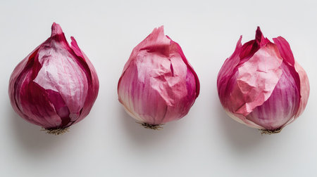 Three whole red onions with their papery outer layers intact, perfectly arranged on a plain white surface.の素材