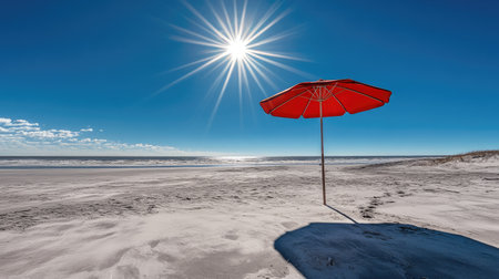 A beach umbrella standing on the sand, surrounded by sunlight, with a brilliant blue sky above.の素材