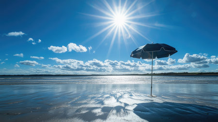A beach umbrella standing on the sand, surrounded by sunlight, with a brilliant blue sky above.の素材