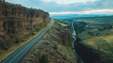 A highway stretching through a green canyon with cascading waterfalls visible on rocky cliffs along the roadの素材