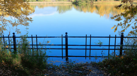 A bleu aluminum fence along the edge of a pristine lake, reflecting the clear blue sky and the surrounding nature.の素材