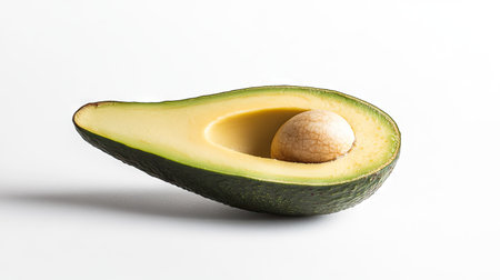 A fresh avocado cut open, the creamy green flesh visible with the pit resting on a white backgroundの素材