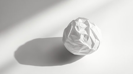 A single ball of wrinkled white paper casting a soft shadow on a plain white surface.の素材