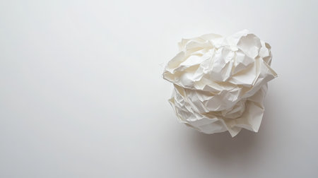 A single, perfectly crumpled paper ball resting on an empty white background, emphasizing simplicity.の素材