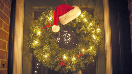 Christmas wreath with sparkling lights, pine needles, and a Santa hat, perfect for welcoming guests in holiday spirit.の素材