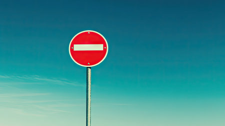 This image depicts a red circular traffic sign with a white horizontal bar, symbolizing no entry. It stands tall against a serene blue sky, representing prohibition.の素材